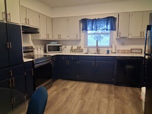 A kitchen with dark blue cabinets, a microwave, a sink, and a window with a blue curtain. - Coastal Escape in the Heart of Morehead City (Morehead City)