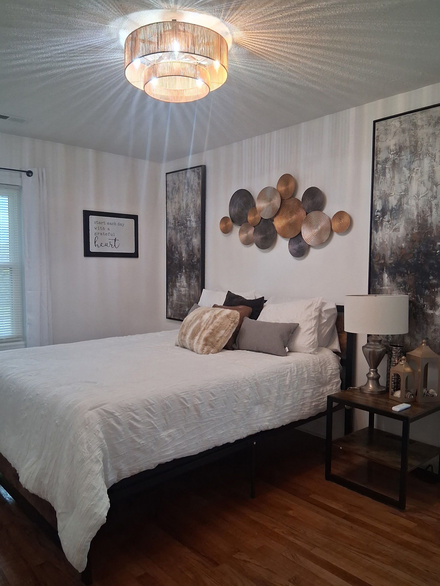 Een slaapkamer met een bed, een nachtkastje, een kunstwerk aan de muur en een plafondlamp.
