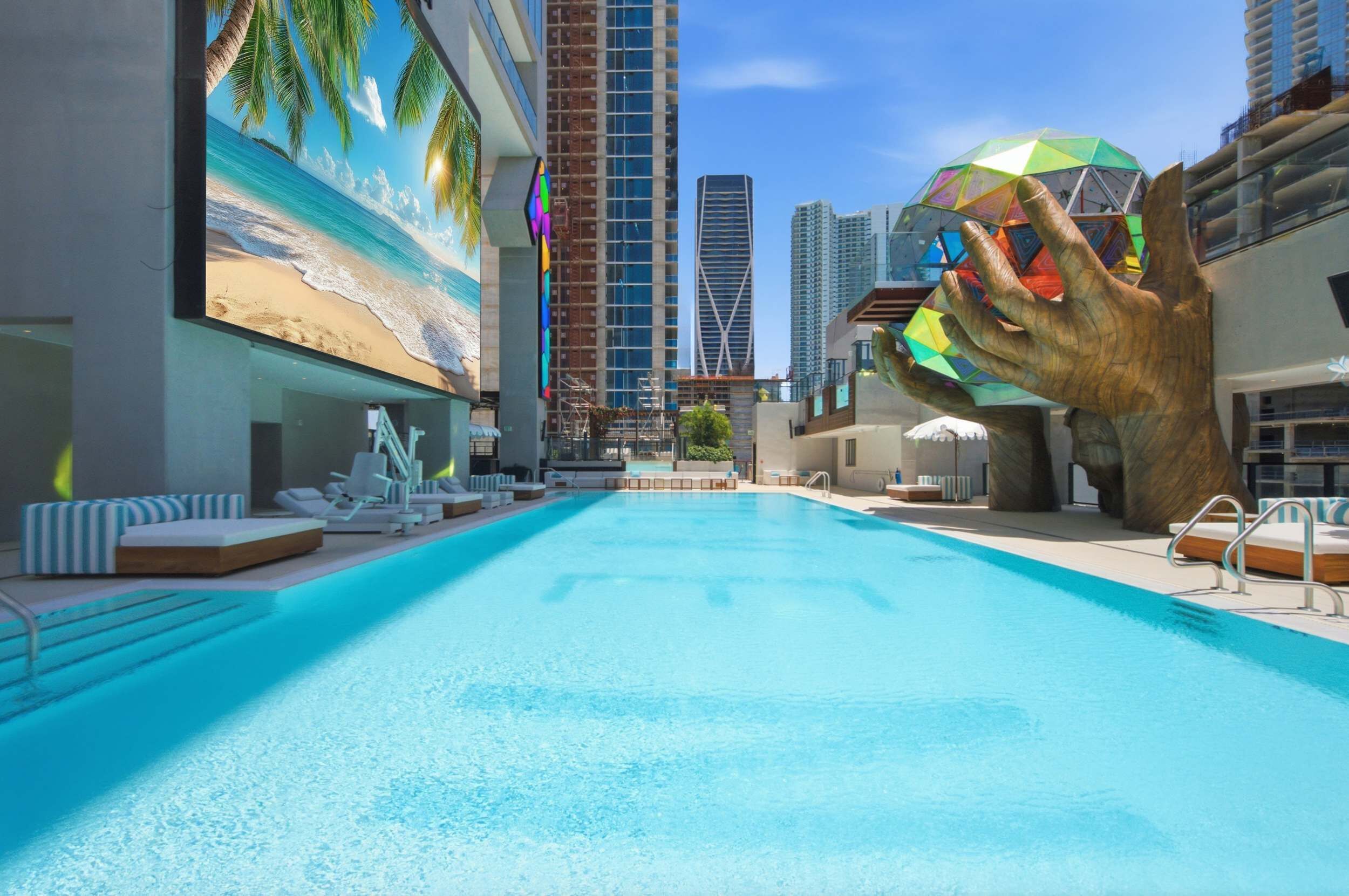 A swimming pool with lounge chairs and a large hand sculpture.