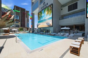 A hotel pool area with lounge chairs, a large screen displaying a beach scene, and a sign reading 'E116 CLUB'. - Deluxe E11EVEN Suite with Elite Amenities (Miami)