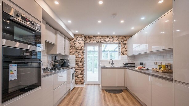 Een moderne keuken met inbouwapparatuur, een accentmuur van steen en uitzicht naar buiten.