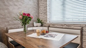 Een houten eettafel met een bloevas, een kop koffie en croissants.