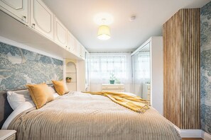 Ein Schlafzimmer mit Bett, Nachttisch, Kommode, Fenster mit Jalousien und einer Wand mit einer vertikalen Holzvertäfelung.