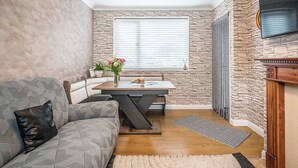 Een gezellige, compacte ruimte met een eettafel, een bank, een open haard en een stenen muur.