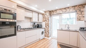 Een moderne keuken met witte kastjes, een inbouwoven, een koffiezetapparaat en een accentmuur van steen.