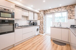 Eine moderne Küche mit weißen Schränken, einem eingebauten Backofen, einer Kaffeemaschine und einer Wand mit Steinverkleidung.