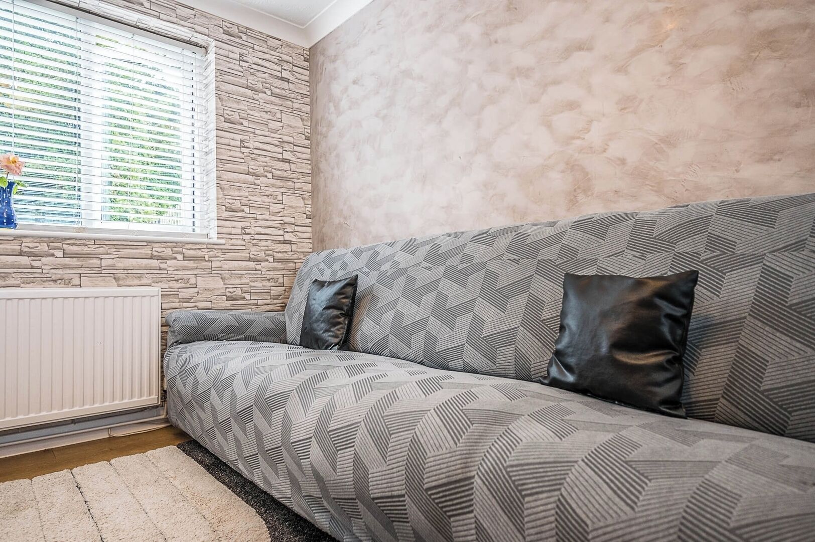 Una sala de estar moderna con una pared de acento de piedra, un sofá estampado y un radiador.