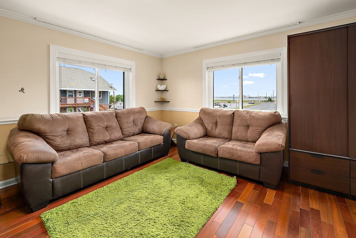 A living room with two brown leather sofas, a green rug, wooden flooring, and a large window with a view.