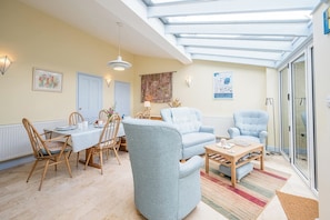 A living room with a dining area, a blue sofa, a wooden coffee table, and a skylight.