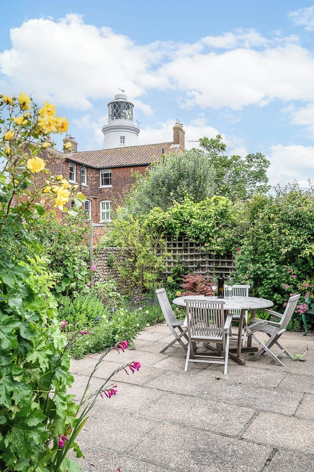Een tuin met een tafel en stoelen, een stenen huis en een watertoren op de achtergrond.