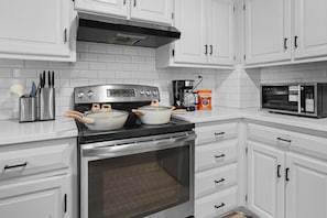 A kitchen with white cabinets, a stainless steel stove, a coffee maker, and a microwave.