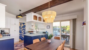 Una cucina moderna con mobili bianchi, un'isola blu e un'area pranzo con tavolo in legno e sedie arancioni.