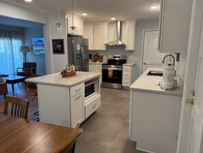 A modern kitchen with white cabinetry, stainless steel appliances, and a dining area with a wooden table and chairs.