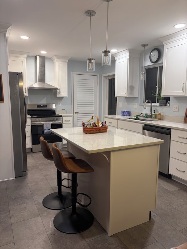 A modern kitchen with stainless steel appliances, a central island with bar stools, and pendant lighting.