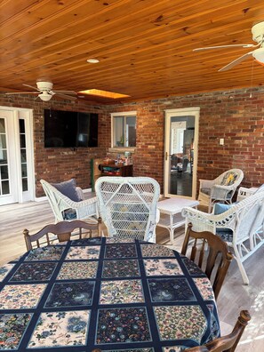 Un patio acogedor con techo de madera, pared de ladrillo, mobiliario de mimbre y una mesa con mantel floreado.