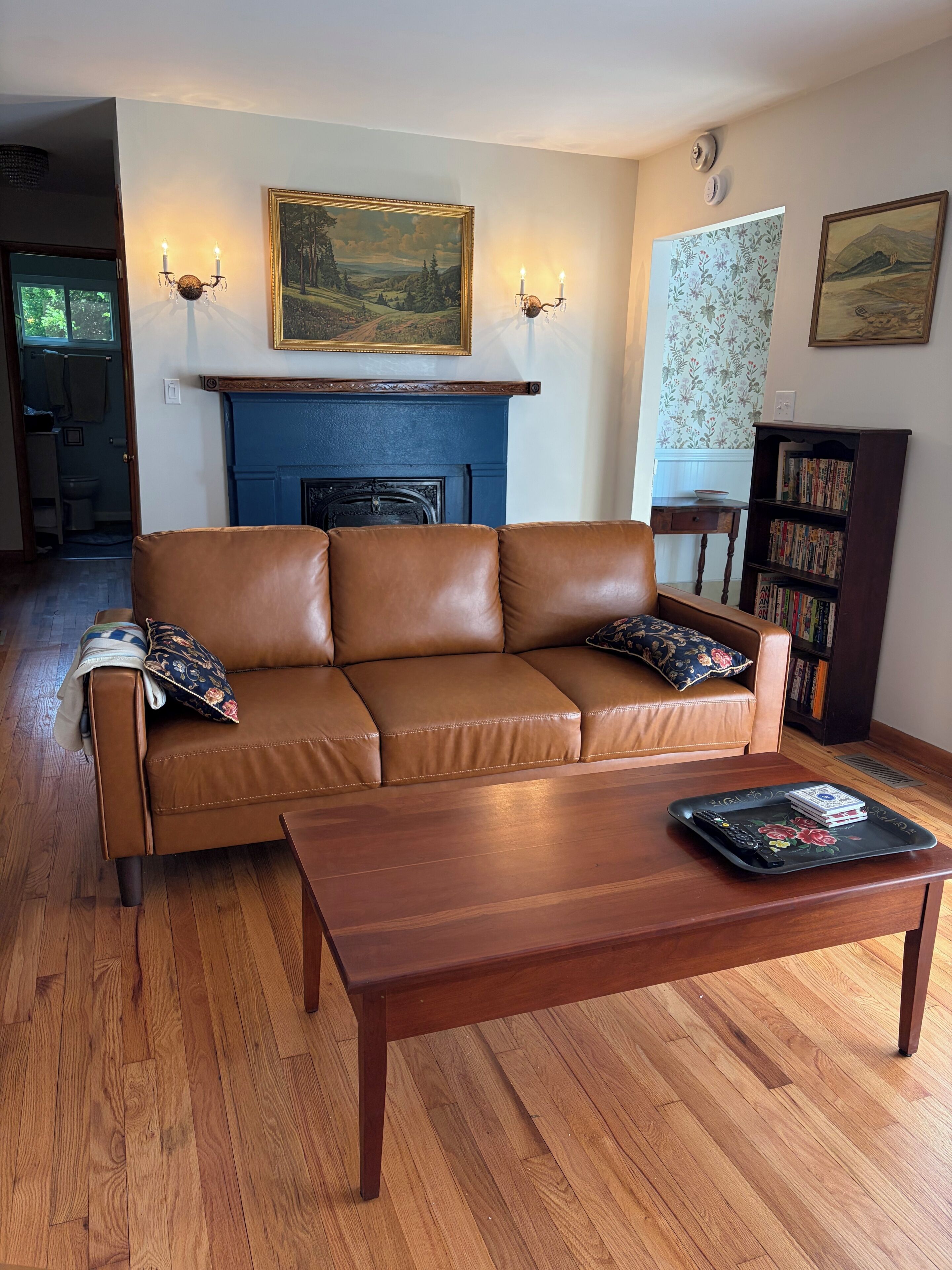 Una sala de estar con un sofá de cuero marrón, una mesa de centro de madera, una chimenea y una estantería.