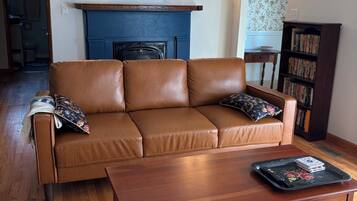 Una sala de estar con un sofá de cuero marrón, una mesa de centro de madera, una chimenea y una estantería.