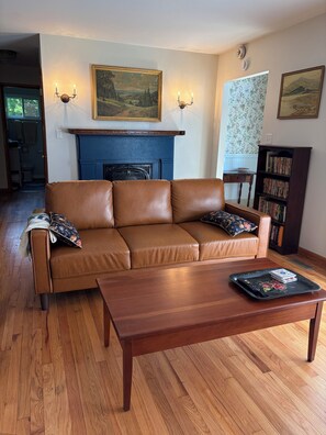 A living room with a brown leather sofa, a wooden coffee table, a fireplace, and a bookshelf.