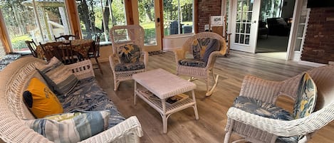A covered patio area with wicker furniture, a coffee table, and a view of the outdoors.
