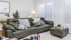 Ein Wohnzimmer mit einem grünen Sofa, einem Beistelltisch mit Lampe und einem Fenster mit transparenten Vorhängen.