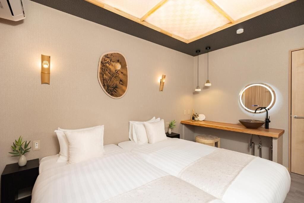 A modern hotel room with a large bed, bedside tables, a vanity with a mirror, and a ceiling light fixture.