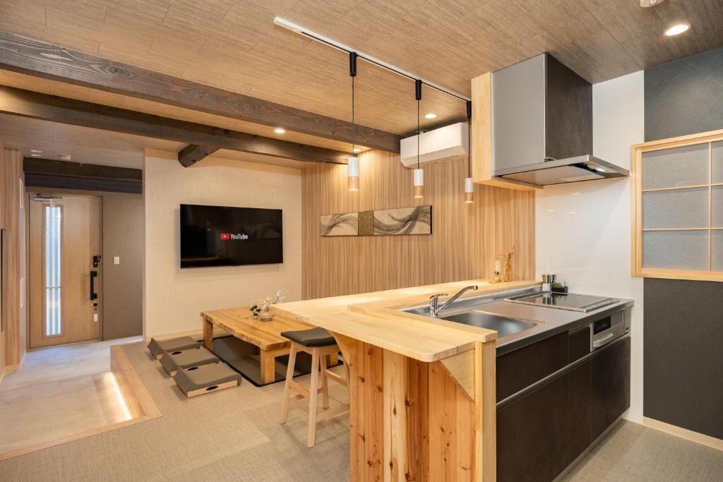 A modern kitchen with wooden cabinetry, a built-in island with a sink, and a flat-screen TV mounted on the wall.