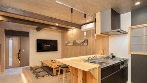 Une cuisine moderne avec des meubles en bois, un îlot central intégré doté d’un évier et un téléviseur à écran plat fixé au mur.