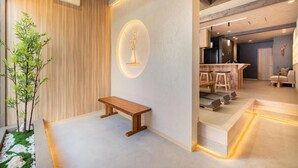 Un intérieur moderne avec un banc en bois, un luminaire fixé au mur et un coin repas comprenant des chaises et une table.