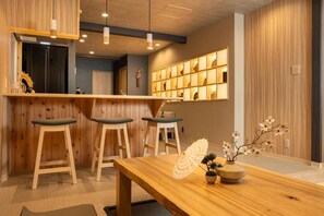 A wooden bar area with stools, a wooden table, and a vase with flowers. - JAPAVISTA Yumeno (BAIKA, KONOHANA WARD)