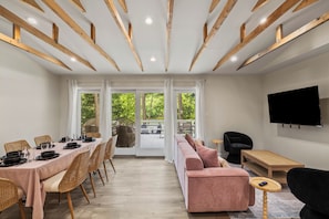 Un salon moderne comprenant un coin repas, des poutres apparentes en bois au plafond, un téléviseur à écran plat et une vue dégagée grâce à de grandes fenêtres.
