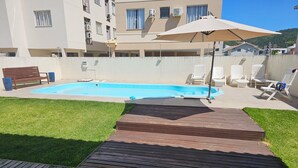 Ein Schwimmbecken mit Holzterrasse, umgeben von Rasen und weißen Stühlen.