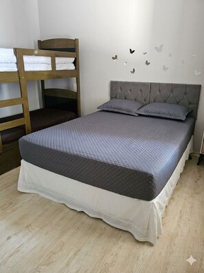 Un dormitorio con una cama litera, una cama con ropa de cama gris, un cabecero tapizado en gris y adhesivos de pared con forma de mariposa.