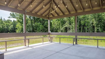Un pavillon ouvert avec un sol en béton, des rampes en métal et un plafond en bois agrémenté de luminaires suspendus.