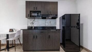 Eine moderne Küche mit dunklen Holzschränken, einer schwarzen Mikrowelle, einem Einbauofen, einem schwarzen Kühlschrank und einer Marmor-Spritzschutzwand.