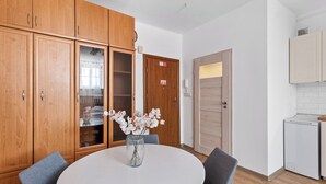 A room with wooden cabinets, a round table with chairs, a vase with flowers, and a door with a sign.