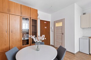 A room with wooden cabinets, a round table with chairs, a vase with flowers, and a door with a sign.