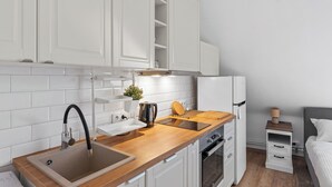 A compact kitchen with white cabinets, a wooden countertop, a sink, a kettle, and a small table.