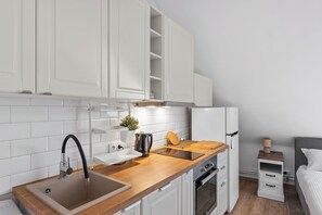 A compact kitchen with white cabinets, a wooden countertop, a sink, a kettle, and a small table.