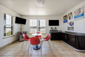 A modern kitchen with a refrigerator, microwave, and coffee maker, a dining area with red chairs and a small table, and a TV mounted on the wall. - Budget-Friendly Stay Close to Sundance Square - 2.4 miles (Fort Worth)