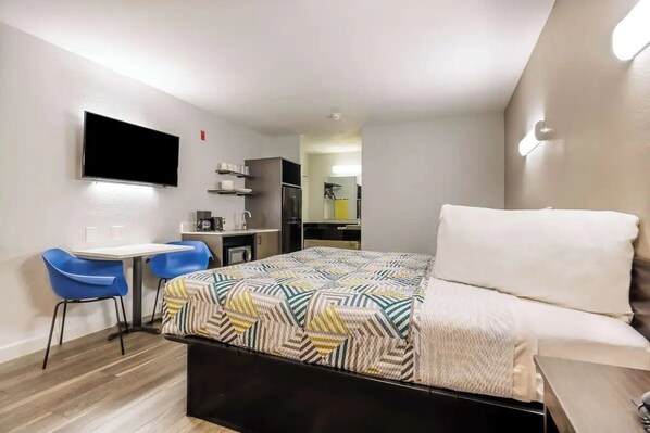 A compact hotel room with a bed, a desk with chairs, a flat-screen TV, and a kitchenette in the background. - Budget-Friendly Stay Close to Sundance Square - 2.4 miles (Fort Worth)