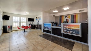 Una zona de recepción con mostrador, sillas, refrigerador y una pared con un cartel.