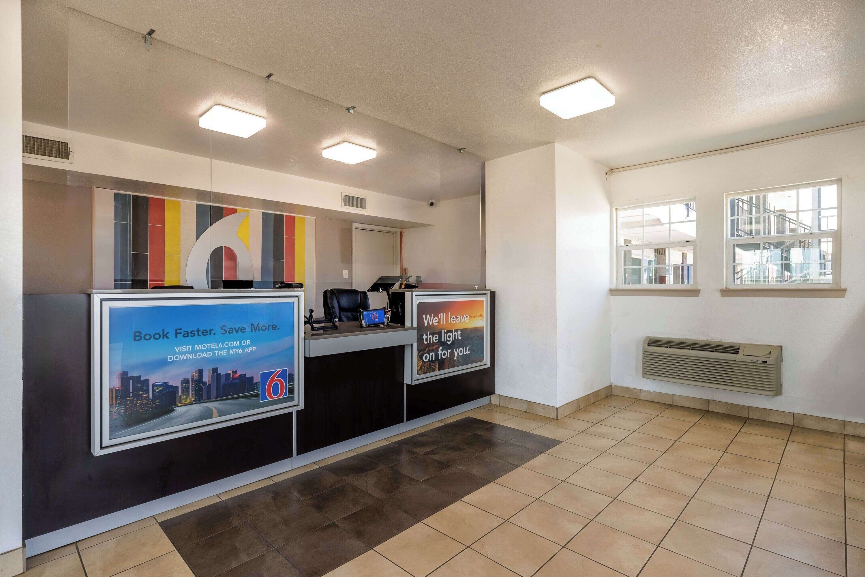A reception desk with a cityscape poster, a digital screen, and a sign about saving money.