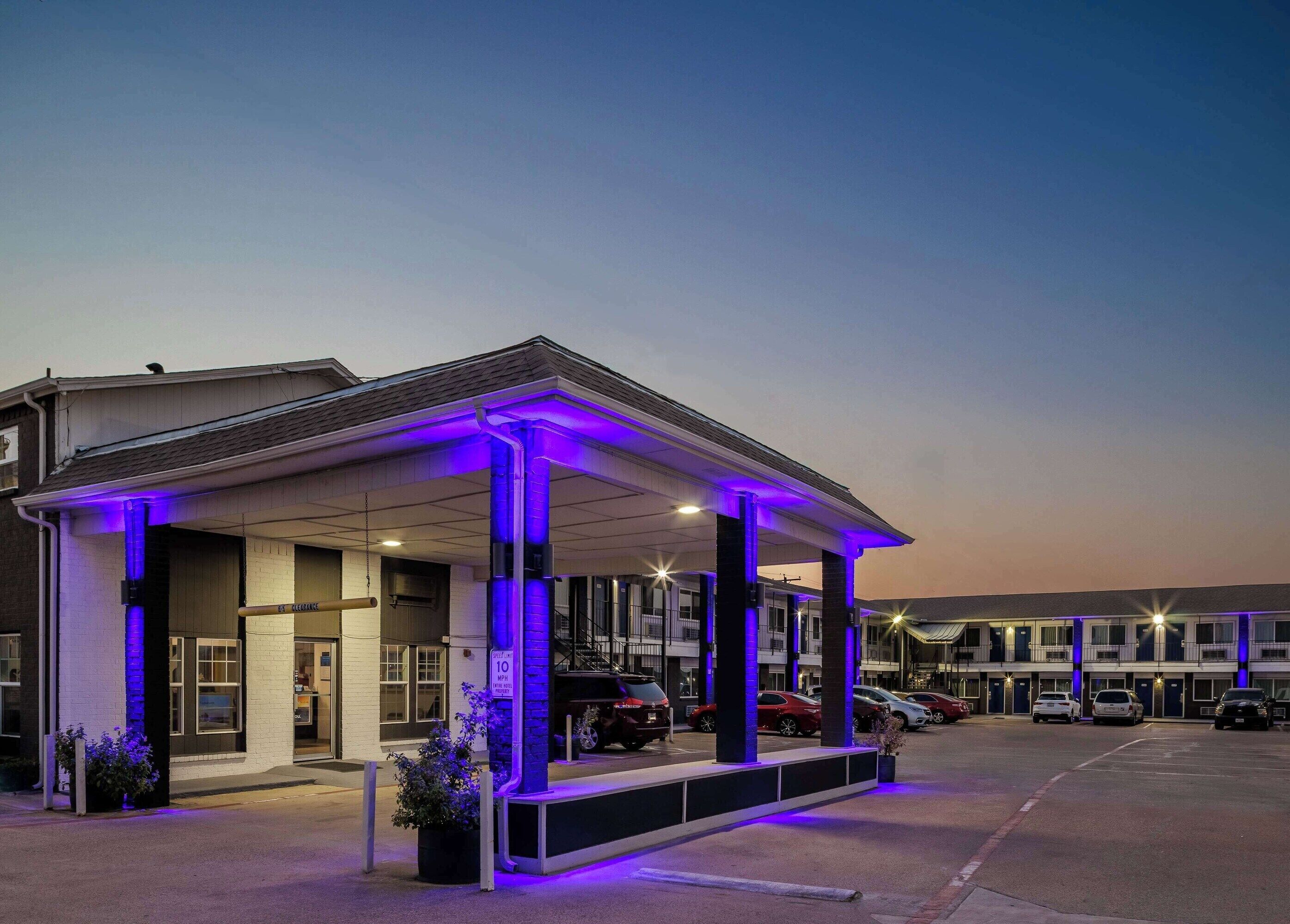 A motel with a covered parking area, multiple cars parked, and a clear sky.