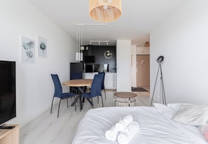 Une chambre d’hôtel moderne avec un lit, un coin repas comprenant des chaises, une petite table ronde, un téléviseur et, au fond, une kitchenette.