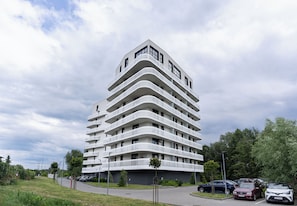 Un immeuble à plusieurs étages doté d’une façade incurvée, d’un espace de stationnement et d’espaces verts.