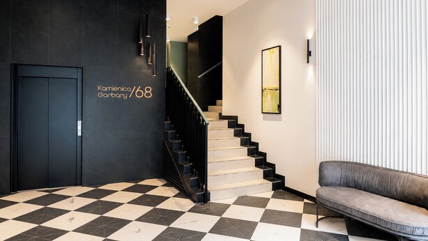 Eine moderne Lobby mit Schachbrettmuster-Boden, einer Treppe, einem Sofa und einem Wandbild.