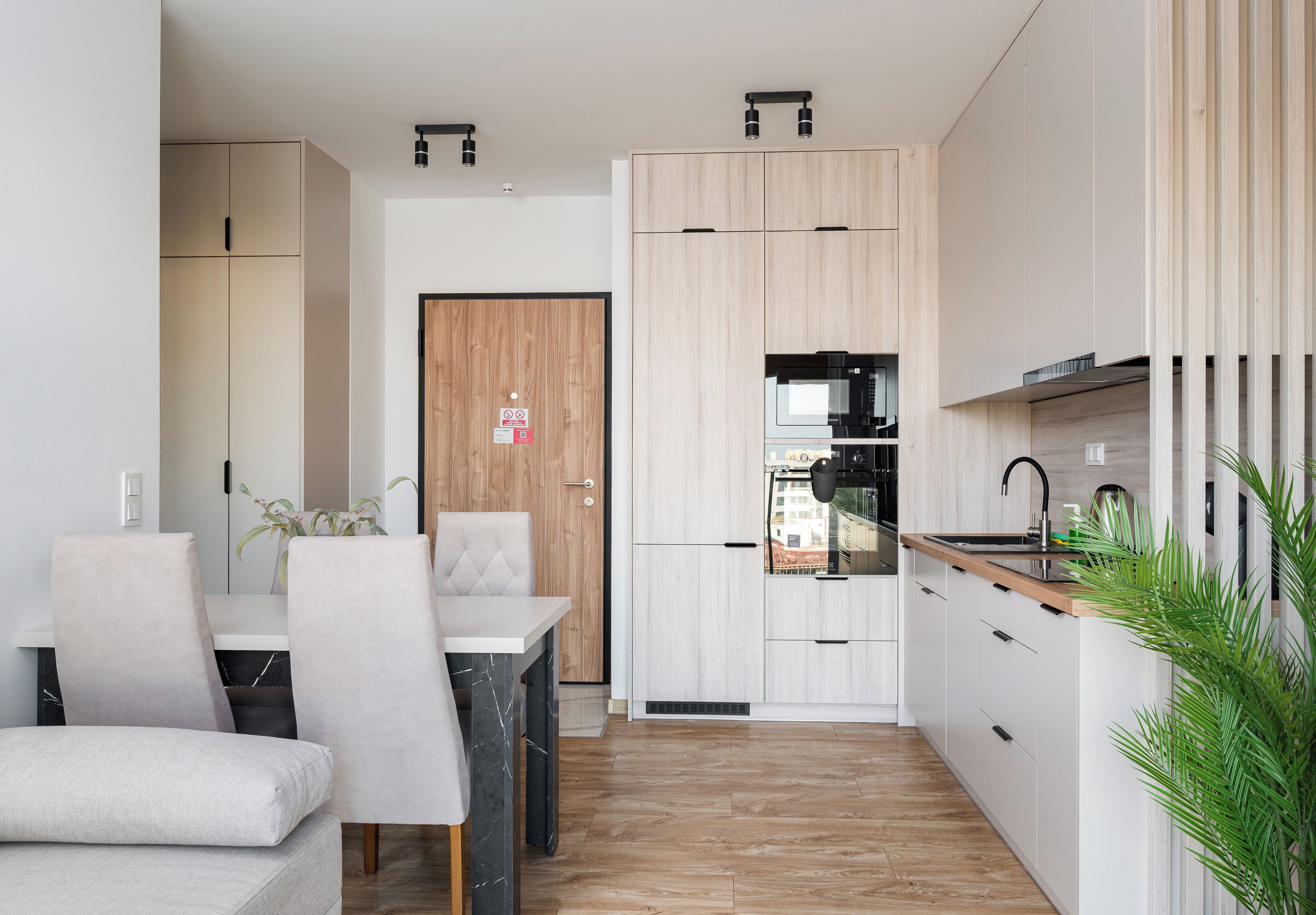 A modern kitchen with built-in appliances, a dining area with a table and chairs, and a wooden door.