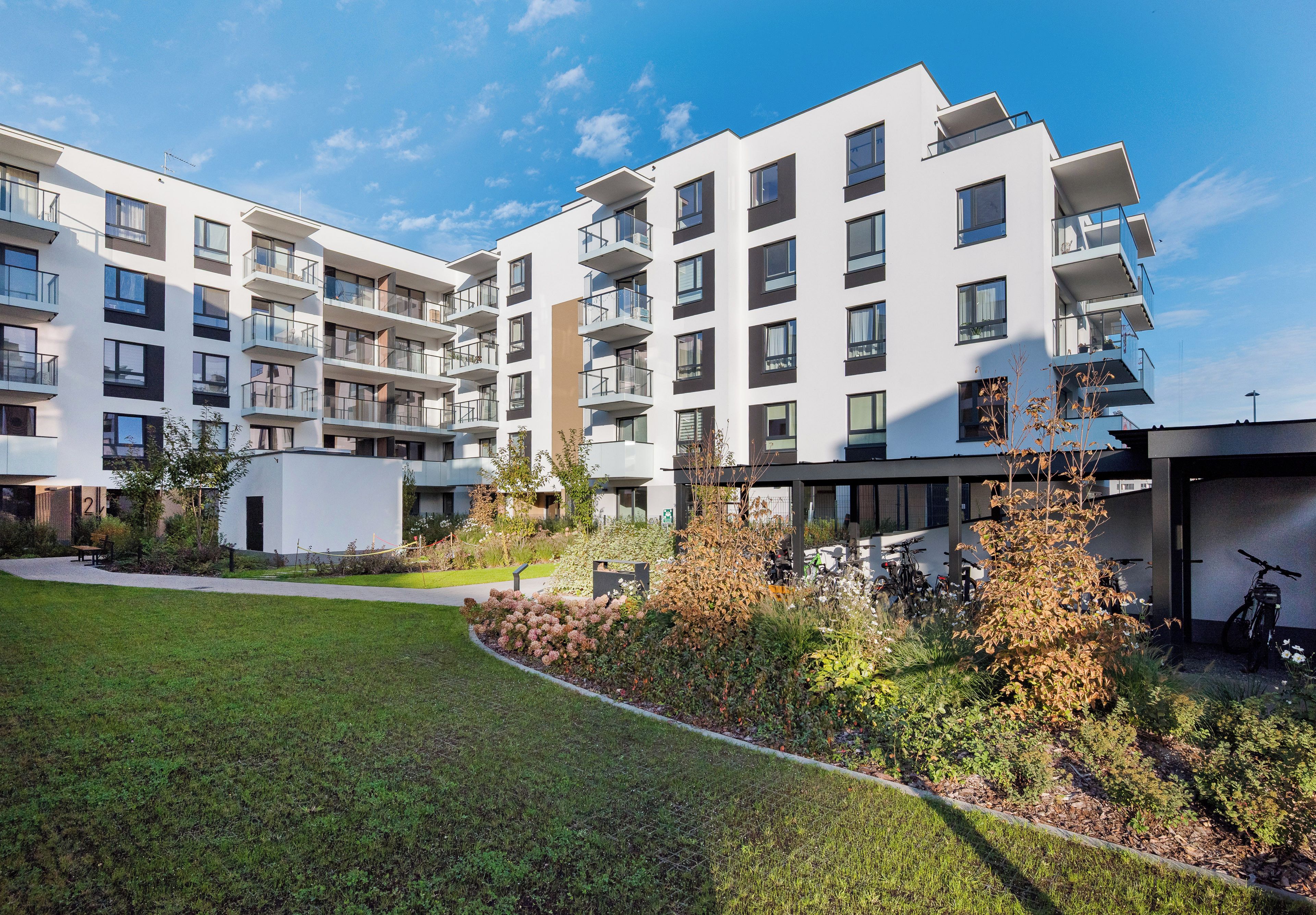 En moderne boligbygning med flere etager, altaner, anlagt have og en klar himmel.