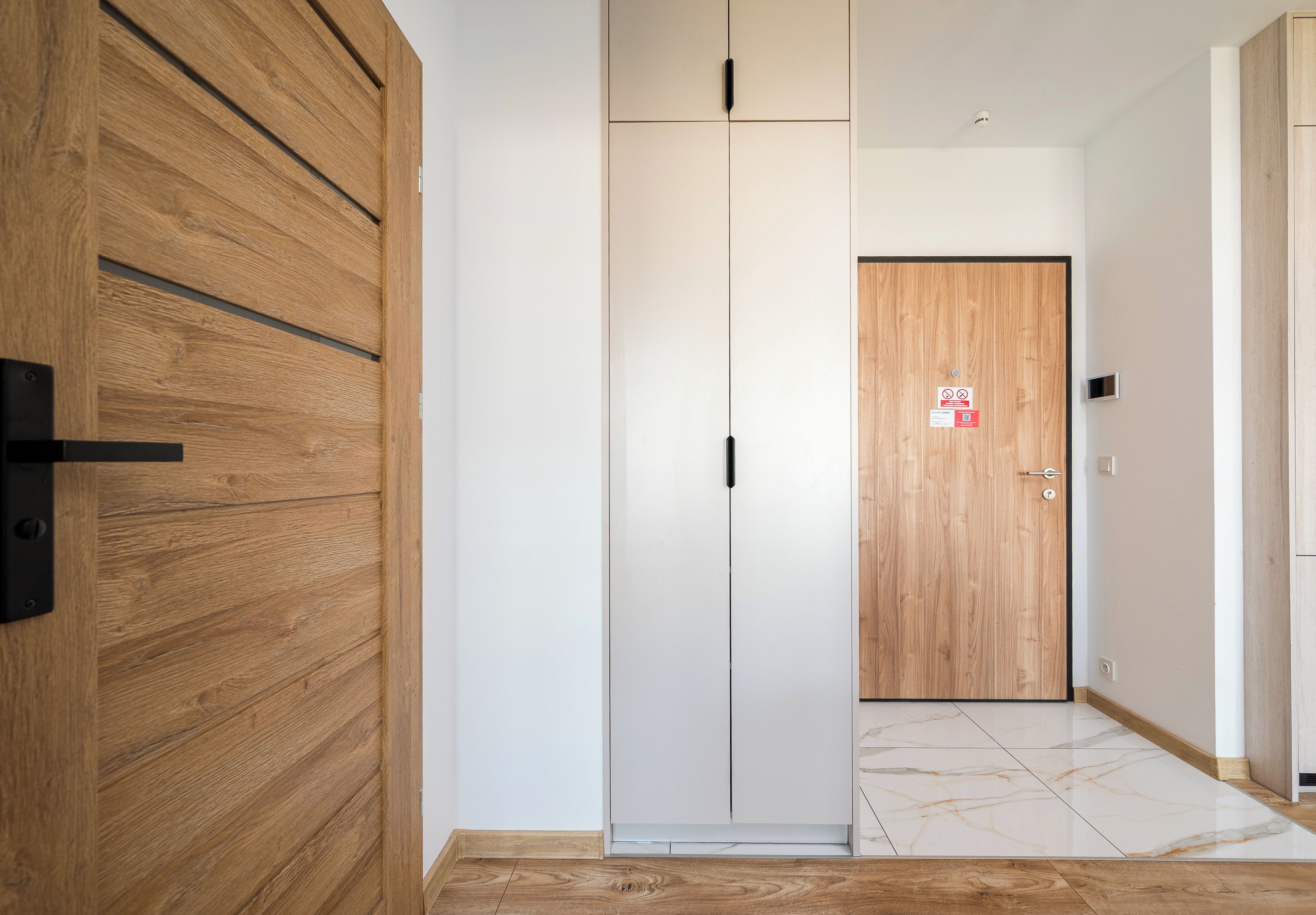 Un corridoio con una porta in legno, una porta bianca con un cartello e un pavimento in marmo.