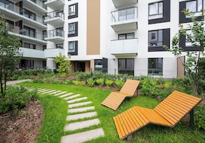 Ein modernes Apartmenthaus mit Innenhof, ausgestattet mit einer Holzbank und einem gepflasterten Weg.